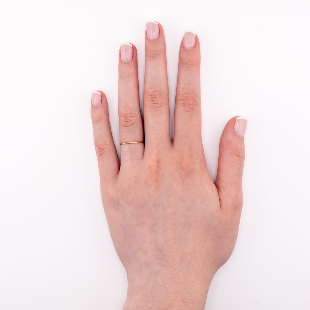 Hand wearing tiny band 14k gold ring on a white background top