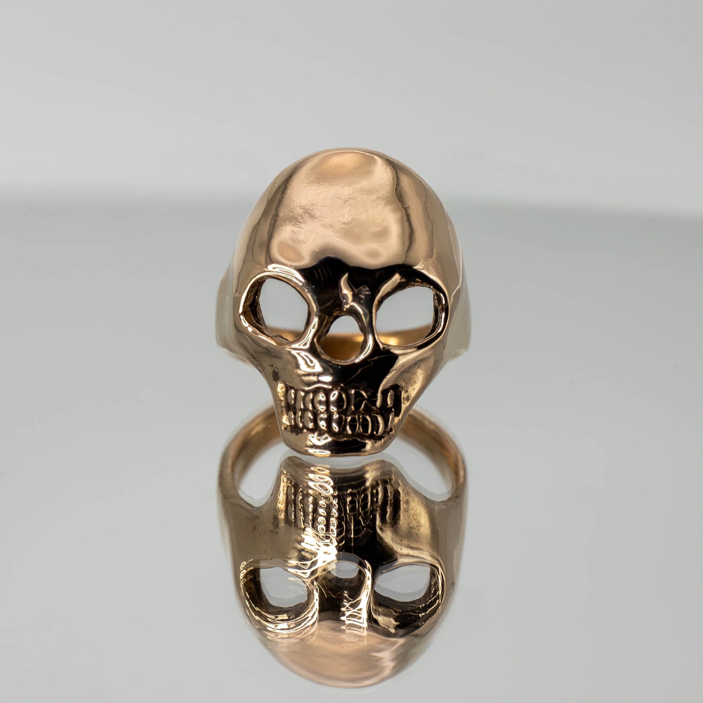 Artistic photo of bronze Skull Ring on mirror surface, handmade in Austin, Texas