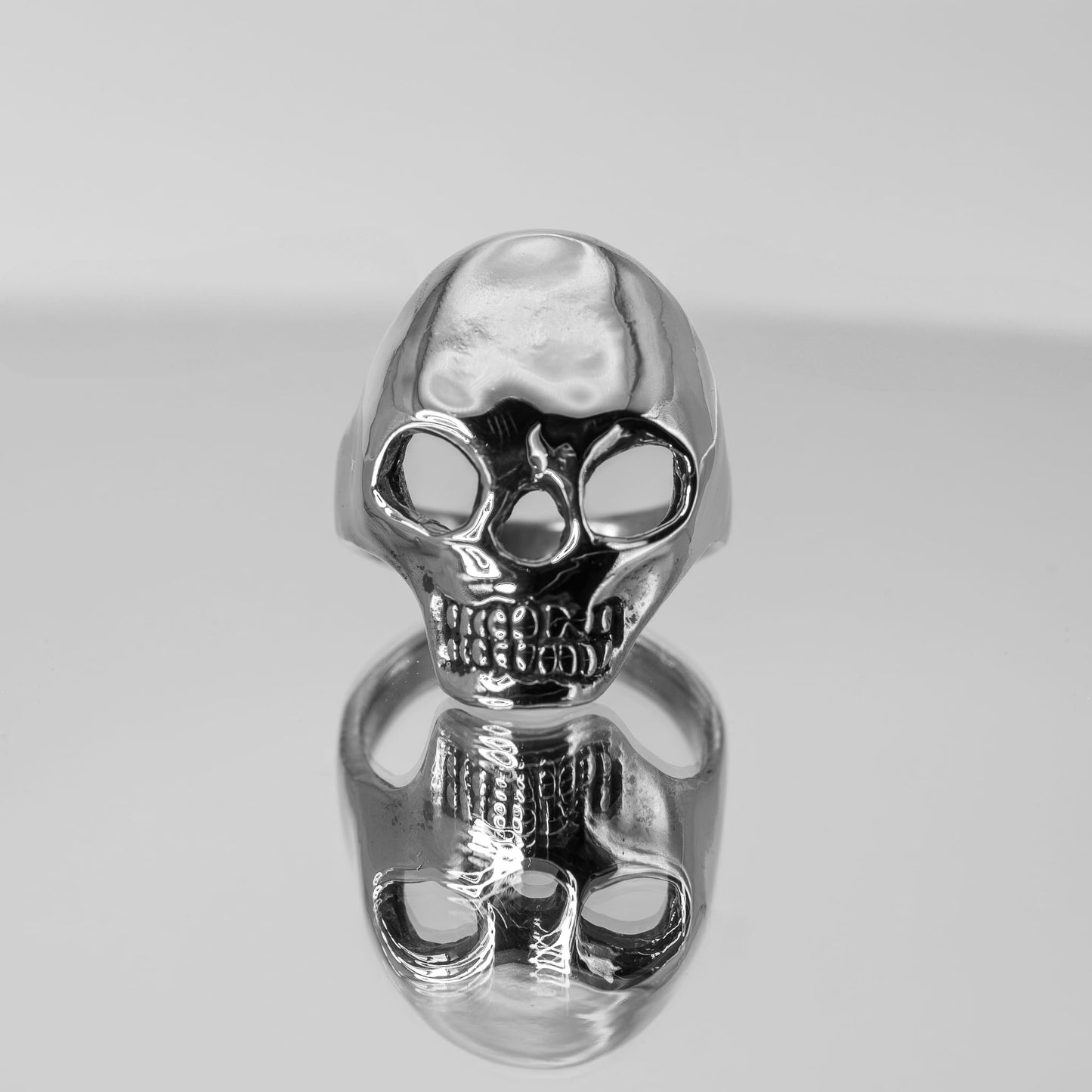 Artistic photo of sterling silver Skull Ring on mirror surface, handmade jewelry crafted in Austin, Texas