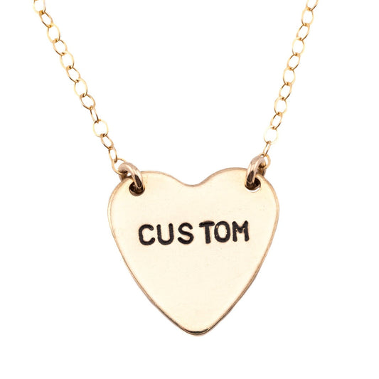 Gold heart-shaped necklace with 'CUSTOM' engraving on a white background