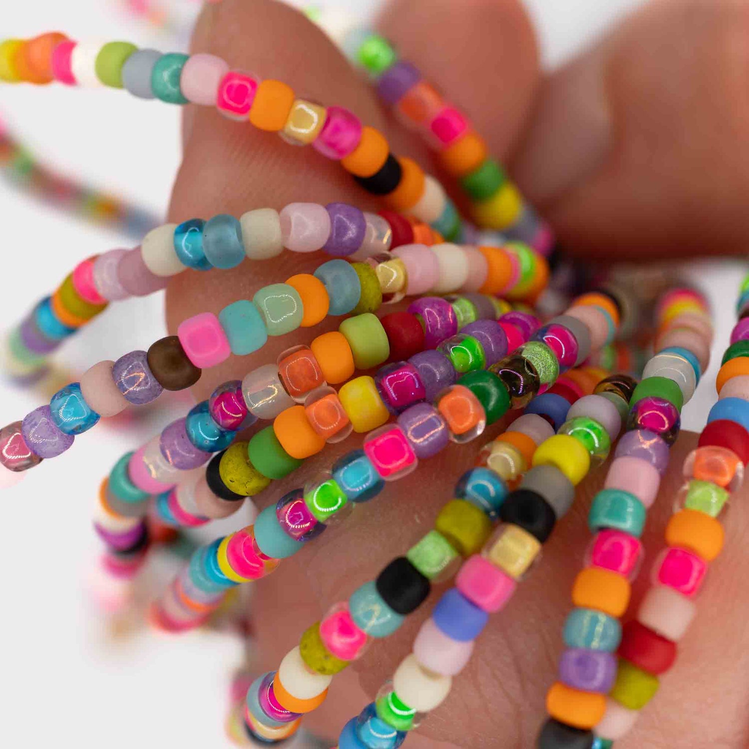 Hand holding multiple Birthday Cake Seed Bead Anklets, colorful handmade glass bead jewelry made in Austin Texas