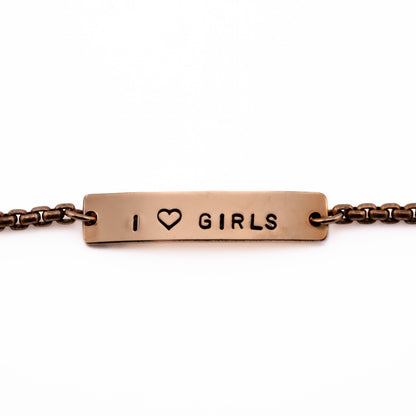 Close-up of I Heart Girls bronze bracelet with stamped heart symbol, lesbian pride