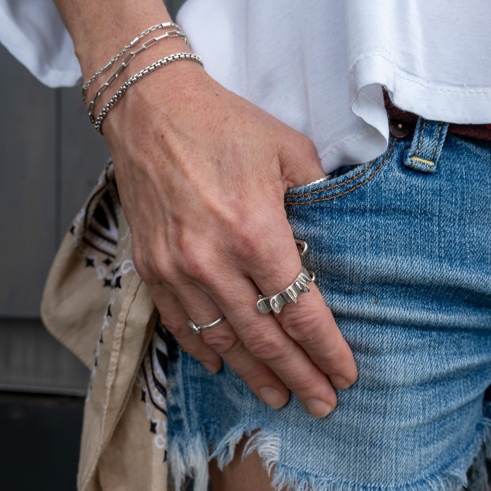 Close-up of salacia ring, a person's hand with multiple silver rings and bracelets, wearing a white shirt and blue jeans.