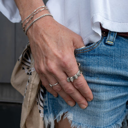 Close-up of salacia ring, a person's hand with multiple silver rings and bracelets, wearing a white shirt and blue jeans.