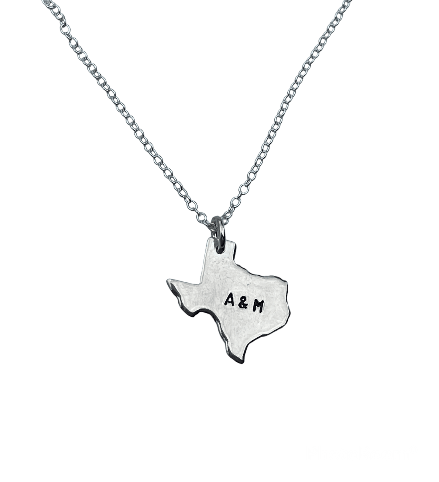A silver chain necklace with a sterling silver pendant in the shape of the state of Texas, with the text 'A&M' hand-stamped on it.